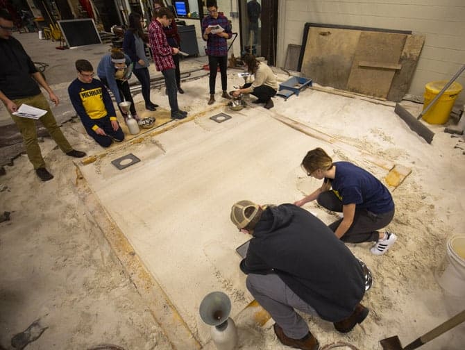 Students kneel by sand pit in a lab