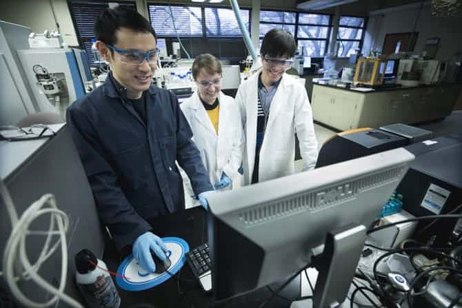 Three people wear saftey goggles and measure data on a computer