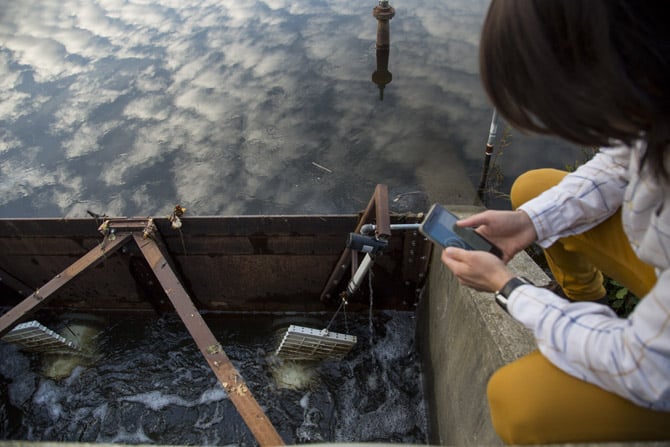 A person crouches before a body of water, in which sensors float.